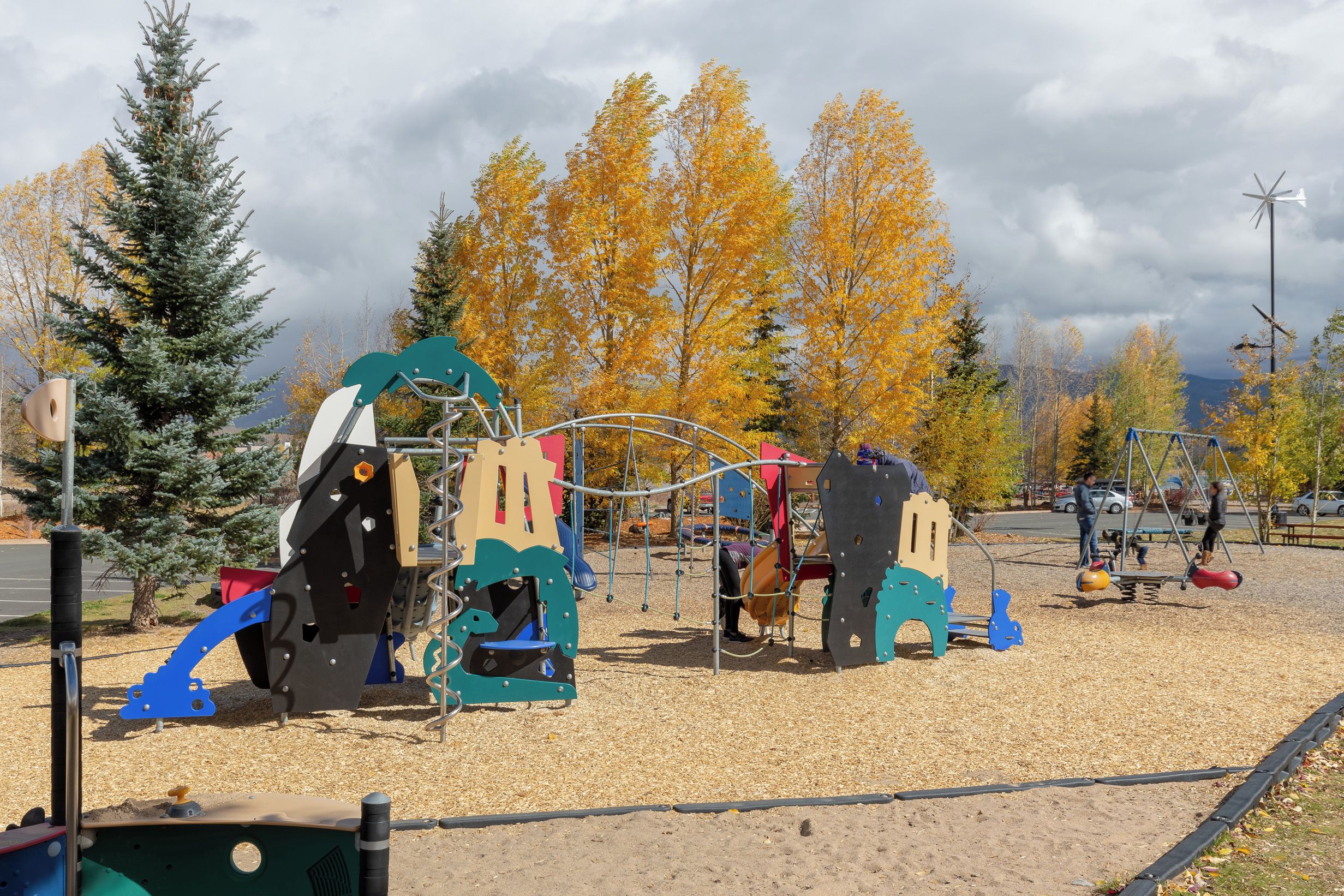 A playground with various play structures, surrounded by trees with autumn foliage.