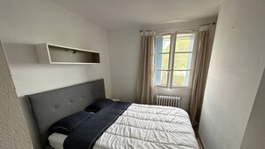 Ett sovrum med en säng, ett sängbord, ett fönster med gardiner och ett element.