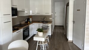 Ett smalt kök med vita skåp, en träbänkskiva och en liten matplats med barstolar.