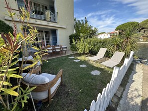 Une terrasse avec des meubles d’extérieur, une clôture blanche et un jardin agrémenté de différentes plantes.