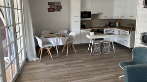 Ett modernt kök med vita skåp, en matplats med bord och stolar samt ett stort fönster med gardiner.