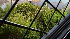 Une vue à travers une fenêtre ornée d’une grille métallique, donnant sur une rivière, de la verdure et des collines lointaines.