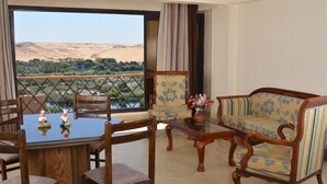 Une pièce comprenant une table à manger, des chaises, un canapé et offrant une vue sur une rivière et des collines.