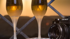 Deux verres de vin blanc sont posés sur une nappe à carreaux, avec un appareil photo et un trépied à proximité.