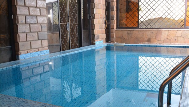 Une piscine intérieure à l’eau d’un bleu cristallin, entourée de murs en pierre et d’une clôture métallique.