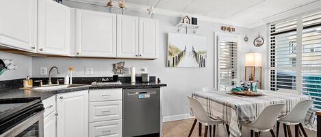 Una cocina moderna con armarios blancos, encimera negra y un comedor con mesa y sillas.