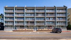 A multi-story building with balconies, a parking lot, and a flag. - Ocean Block 2 BR 2 BA Unit - Short Walk to the Beach! (Ocean City)