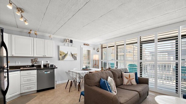A modern kitchen with white cabinets, a dining area with a table and chairs, and a living room with a sofa and a view through large windows. - Ocean Block 2 BR 2 BA Unit - Short Walk to the Beach! (Ocean City)