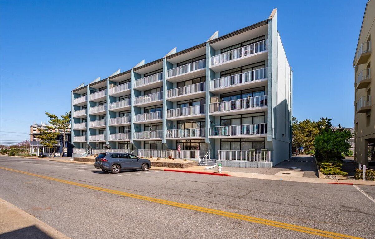 A multi-story hotel with balconies, a parking lot, and a clear sky.