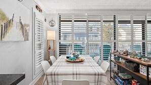 A dining area with a table set for two, a window with blinds, and a bookshelf with various items. - Ocean Block 2 BR 2 BA Unit - Short Walk to the Beach! (Ocean City)