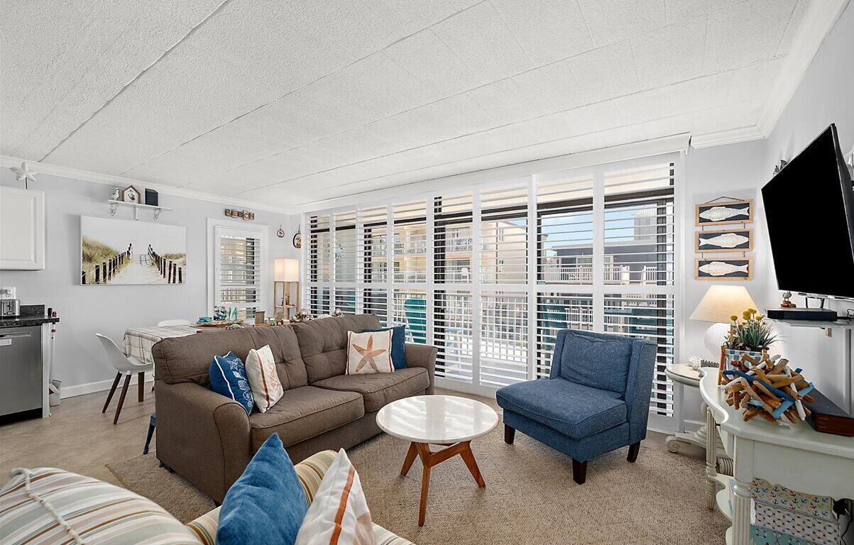A living room with a sofa, armchair, and coffee table, a TV, and a window with blinds.