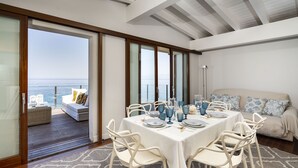 A dining area with a table set for four, white chairs, and a view of the sea through large glass doors. - Rais house with private access to the sea (Solanto)