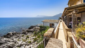 A coastal building with a terrace overlooking the sea, featuring a stone pathway and potted plants. - Rais house with private access to the sea (Solanto)