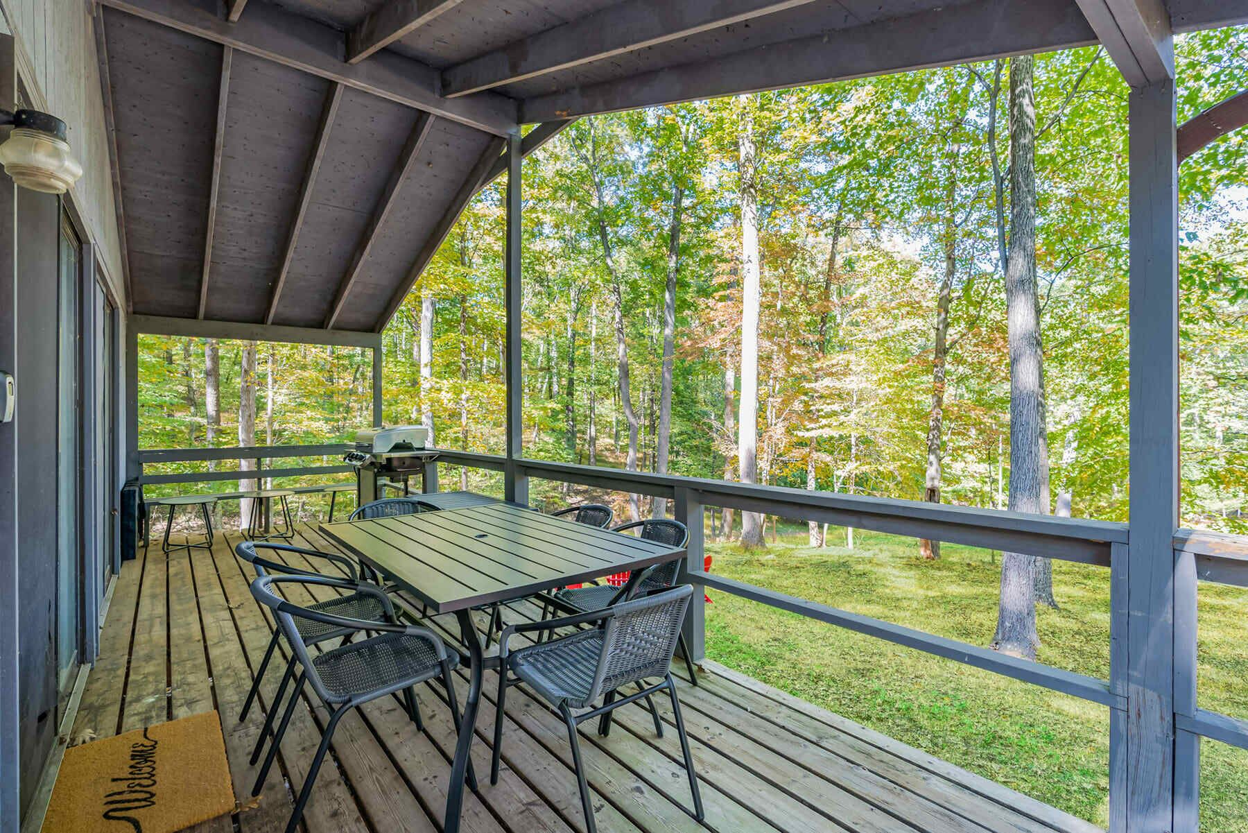 A covered outdoor deck with a table and chairs, overlooking a forested area.