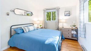 Un dormitorio con cama, mesita de noche, espejo, ventana con cortinas y vistas al exterior.