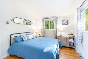 Un dormitorio con cama, mesita de noche, espejo, ventana con cortinas y vistas al exterior.