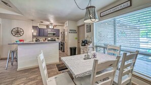 Une cuisine moderne dotée d’un îlot central, d’un coin repas avec une table et des chaises, et d’une grande fenêtre avec des stores.