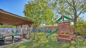 Un jardin avec une structure de jeux en bois, un patio couvert et une table avec des chaises.