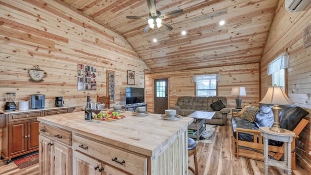 A rustic cabin interior with a wooden interior, a kitchen area with a central island, a sofa, and a dining table. - Benjamin Cabin-HotTub-10 min to Main Street! (Fredericksburg)