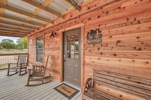 Une cabane en bois avec une véranda, une porte ornée de blasons et deux fauteuils à bascule.
