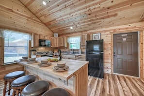 Une cuisine de style rustique, avec des éléments en bois, un îlot central, des tabourets de bar, un réfrigérateur et une porte sur laquelle est apposée une enseigne.