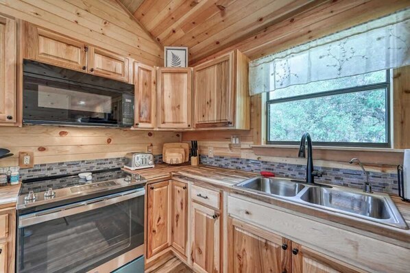 A wooden cabin kitchen with a large window, a built-in oven, and a sink.