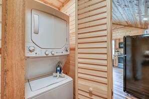 Une cuisine compacte aux murs en bois, dotée d’un lave-linge et d’un sèche-linge intégrés, et d’un réfrigérateur noir.