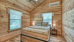 Ein Schlafzimmer einer Holzhütte mit einem Bett, zwei Nachttischen, einem Deckenventilator und zwei Fenstern.