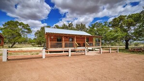 A wooden cabin with a metal roof, surrounded by a fenced area and trees. - Benjamin Cabin-HotTub-10 min to Main Street! (Fredericksburg)