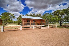 Eine Holzhütte mit einem Metalldach, umgeben von einem eingezäunten Bereich und Bäumen.