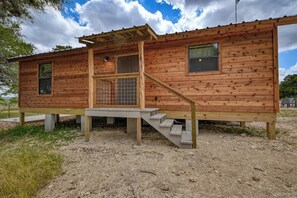 Une cabane en bois dotée d’un porche couvert, d’une petite fenêtre et d’une porte avec un portail en métal.