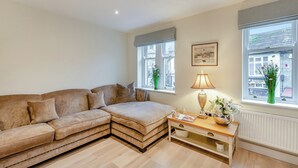 A cozy living room with a beige sectional sofa, a wooden coffee table, and a window with a view of buildings. - Market Square is a cosy, well-equipped holiday home. (Grassington)