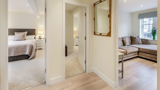 A modern bedroom with a bed, bedside tables, and a large mirror. - Market Square is a cosy, well-equipped holiday home. (Grassington)