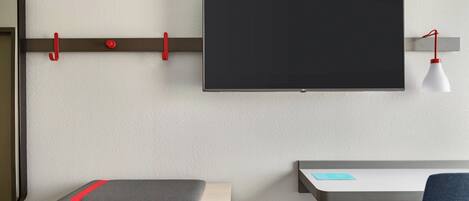 Una habitación moderna con un televisor de pantalla plana montado, un escritorio con silla y una estantería con cojín.