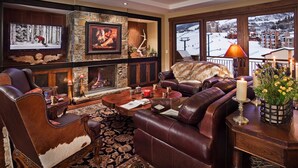 Ein gemütliches Wohnzimmer mit Ledersofas, einem Kamin und einem großen Fenster mit Blick auf eine verschneite Landschaft.