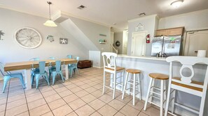 A kitchen with a dining table, chairs, bar stools, a refrigerator, and a clock on the wall.