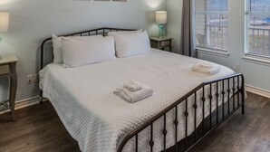 Une chambre à coucher comprenant un lit, un ventilateur de plafond, une fenêtre avec des stores et une table de chevet avec une lampe.