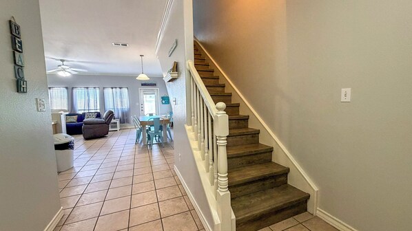 A staircase leading to a second floor, a dining area with a table and chairs, and a living room with a sofa and a ceiling fan. - Coastal Escape | Heated Pool, Patio & Balcony (Corpus Christi)