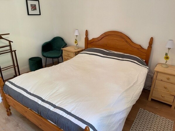 Un lit bien fait, avec une tête de lit en bois, une chaise verte, des tables de chevet avec des lampes et un tableau encadré au mur.