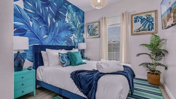 Een slaapkamer met een grote muurschildering van een tropisch blad, een bed met witte lakens, blauwgroene kussens en een gestreept vloerkleed.