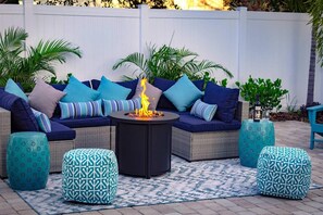 A cozy outdoor seating area with a fire pit, cushioned sofas, and patterned ottomans.