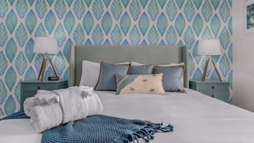 A neatly made bed with a blue blanket and pillows, two bedside tables with lamps, and a patterned wallpaper.