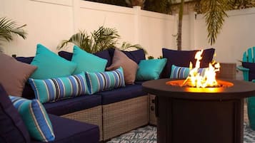 An outdoor seating area with a fire pit, cushioned seating, and a white fence.