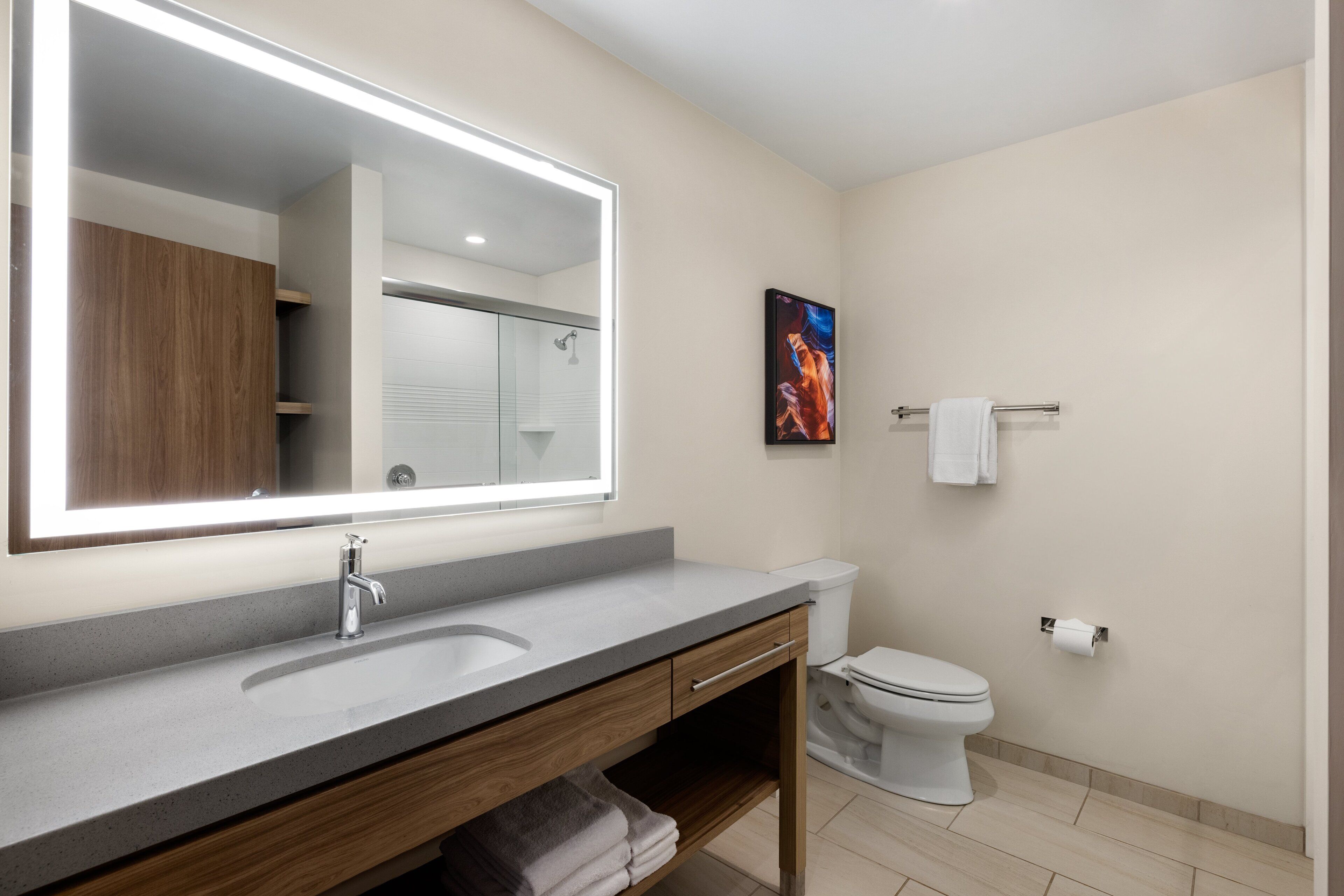 A modern bathroom with a large mirror, a sink, a toilet, and a towel rack.