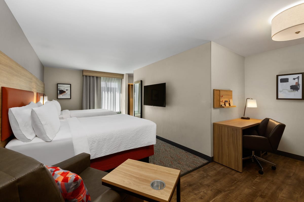 A hotel room with a bed, a desk, a chair, a TV, and a window with curtains.