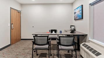 Un salón de conferencias con una mesa larga, cuatro sillas, un proyector, una máquina de café y un cuadro colgado en la pared.