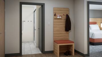 Habitación de hotel con un banco de madera, una cama con colcha estampada y una puerta que da a un pasillo.