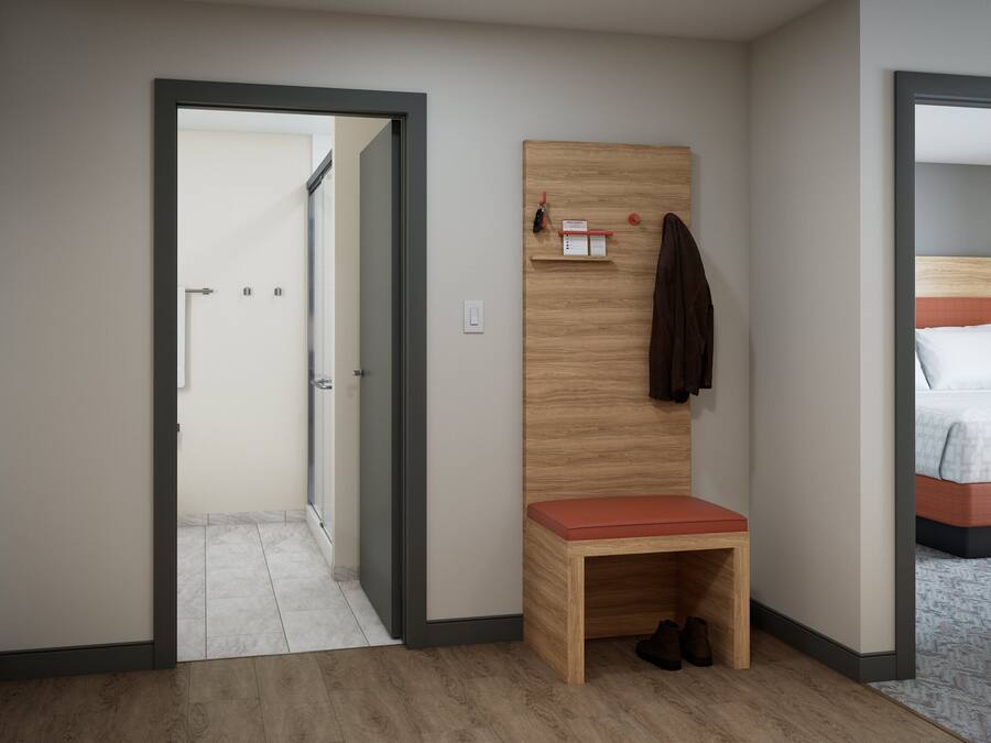 Habitación de hotel con un banco de madera, una cama con colcha estampada y una puerta que da a un pasillo.
