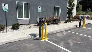 Estaciones de carga para vehículos eléctricos con señalización de estacionamiento, un edificio con ventanas amplias y una zona de estacionamiento pavimentada.