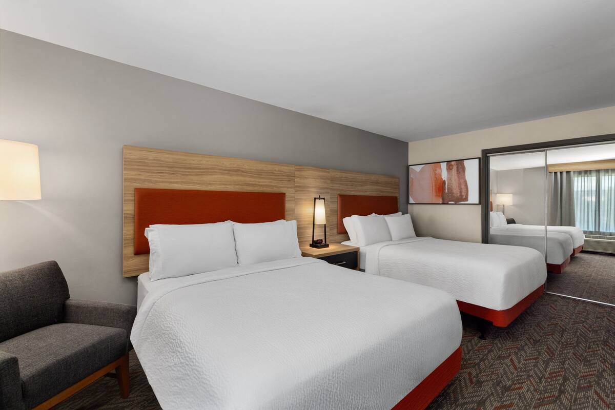 A hotel room with two beds, a sofa, a nightstand, and a mirror.